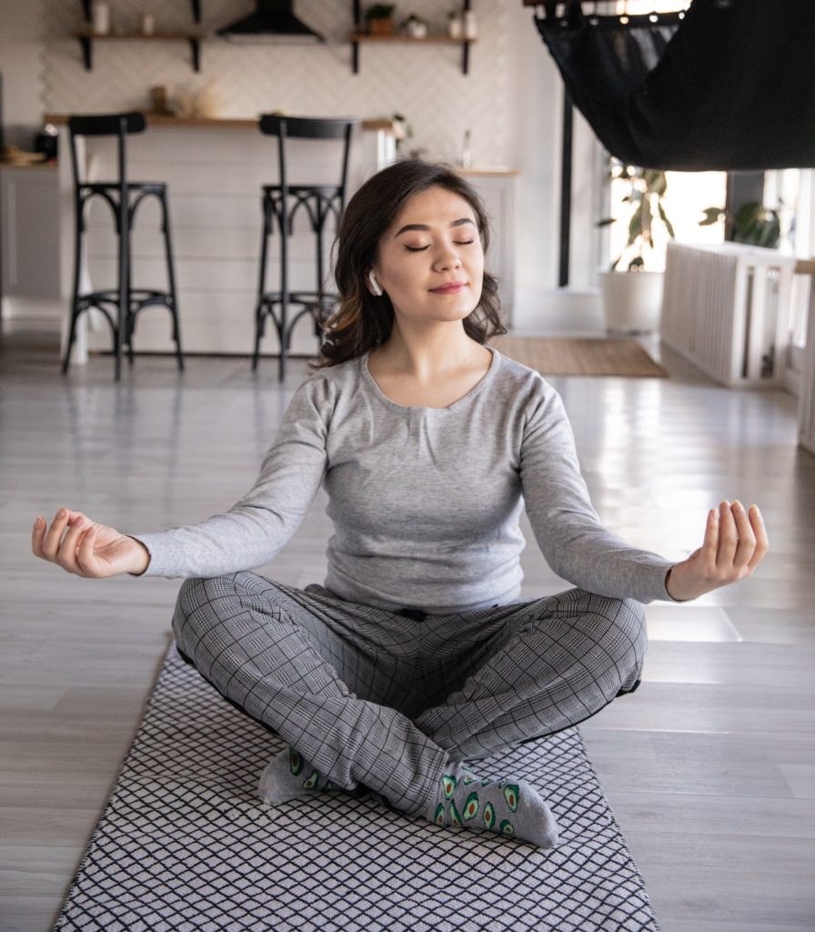 Woman sits on mat and meditates with music from earbuds