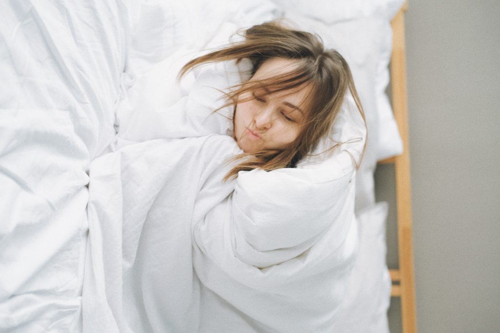 Woman sleeps fully covered in white weighted blanket and sheets